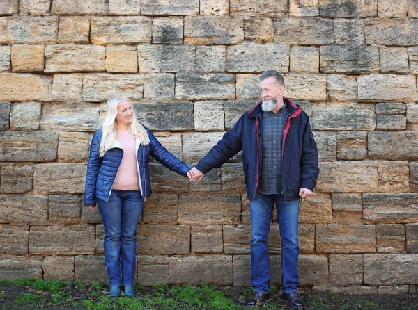 Feliz pareja madura cogida de la mano cerca de la pared de ladrillo al aire libre — Foto de Stock