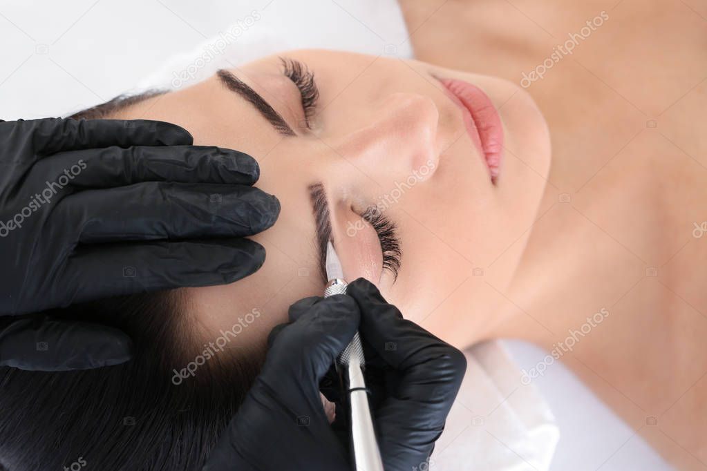 Young woman undergoing procedure of eyebrow permanent makeup in beauty salon, closeup
