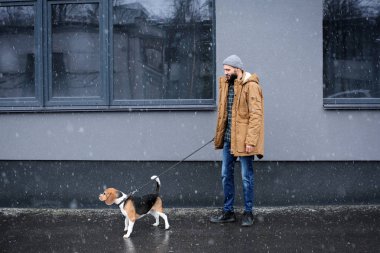 Yakışıklı genç hipster köpeğini açık havada karlı gününde yürüyüşe