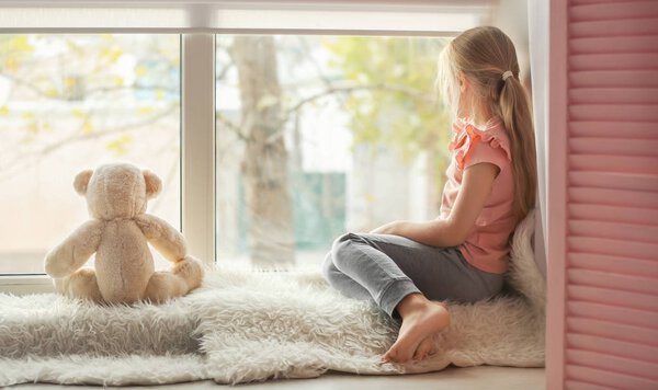 Little girl with teddy bear sitting on window sill. Autism concept