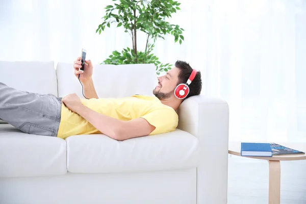 Junger Mann hört Musik, während er es sich zu Hause auf dem Sofa gemütlich macht — Stockfoto