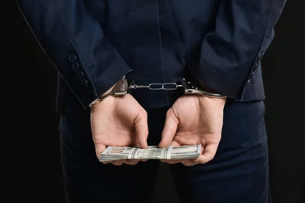 Бізнесмен в наручниках тримає хабар на чорному тлі, крупним планом — стокове фото