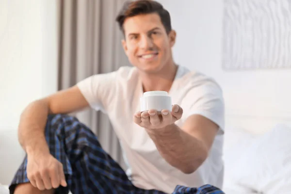 Joven guapo con tarro de crema en casa — Foto de Stock