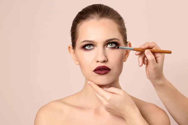Professionele visage kunstenaar toepassing van make-up op vrouw gezicht op lichte achtergrond — Stockfoto