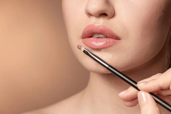 Professionele visage kunstenaar toepassing van make-up op vrouw gezicht op kleur achtergrond — Stockfoto