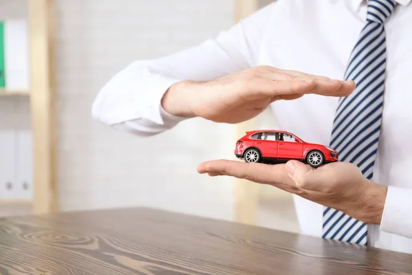 Man in office wear protecting car model. Vehicle insurance — Stock Photo, Image