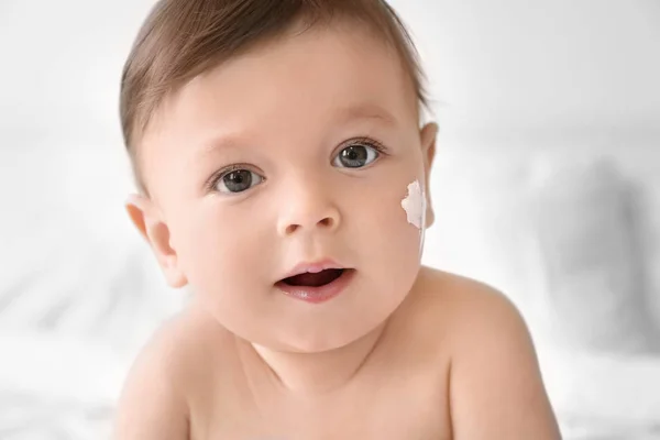 Bebê bonito com creme corporal na bochecha contra fundo claro — Fotografia de Stock