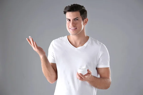 Schöner Mann mit einem Glas Körpercreme auf grauem Hintergrund — Stockfoto