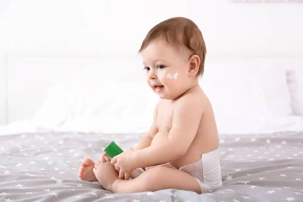 Bebê bonito com garrafa de creme corporal na cama — Fotografia de Stock
