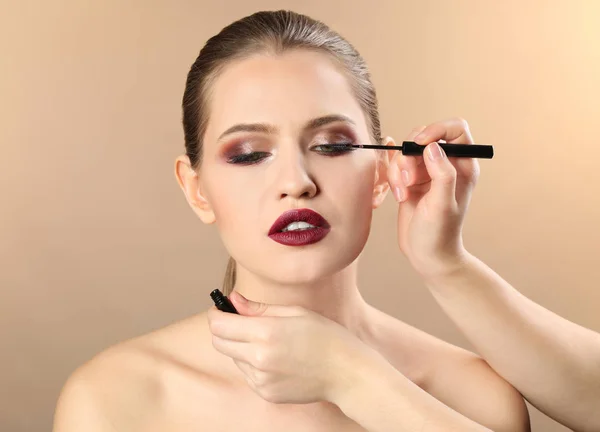 Professional visage artist applying makeup on woman's face on color background — Stock Photo, Image