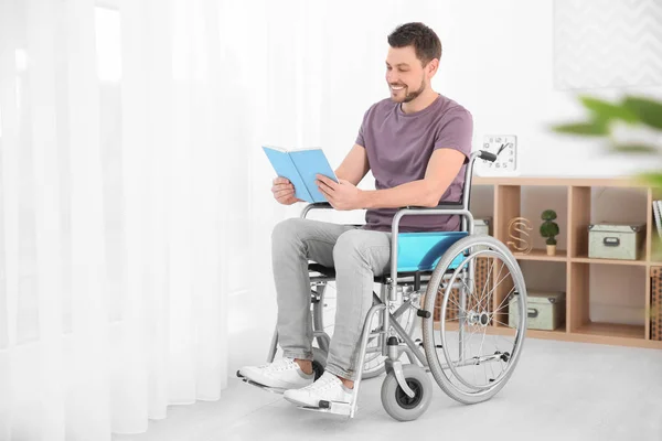 Молодий чоловік у інвалідному візку читає книгу в приміщенні — стокове фото