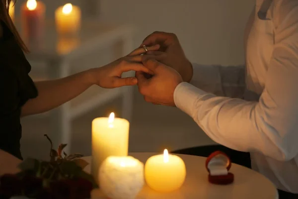 Muž uvedení zásnubní prsten na prst snoubenky zatímco sedí u stolu s hořící svíčky — Stock fotografie