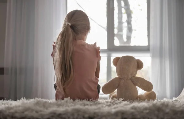 Маленька дівчинка з плюшевим ведмедем сидить на підлозі в кімнаті. Концепція аутизму — стокове фото