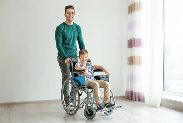 Jonge man het verzorgen van kleine jongen in de rolstoel binnenshuis — Stockfoto