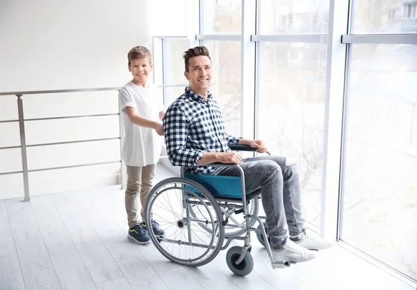 Het verzorgen van jonge man in rolstoel binnenshuis jongetje — Stockfoto
