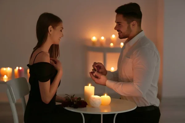 Joven con anillo de compromiso haciendo propuesta a su novia mientras está sentado en la mesa con velas encendidas — Foto de Stock