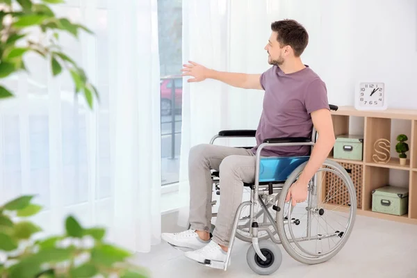 Joven en silla de ruedas cerca de la ventana interior — Foto de Stock