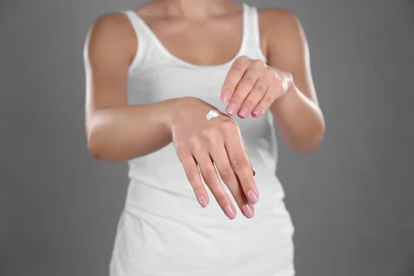 Mujer joven aplicando crema de manos sobre fondo gris — Foto de Stock