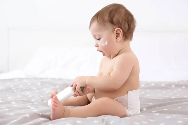 Cute baby with bottle of body cream on bed — Stock Photo, Image