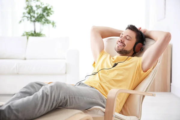 Junger Mann hört Musik, während er es sich zu Hause im Sessel gemütlich macht — Stockfoto