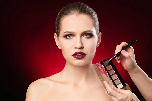 Professionell visage konstnären tillämpa makeup på kvinnans ansikte på mörk bakgrund — Stockfoto