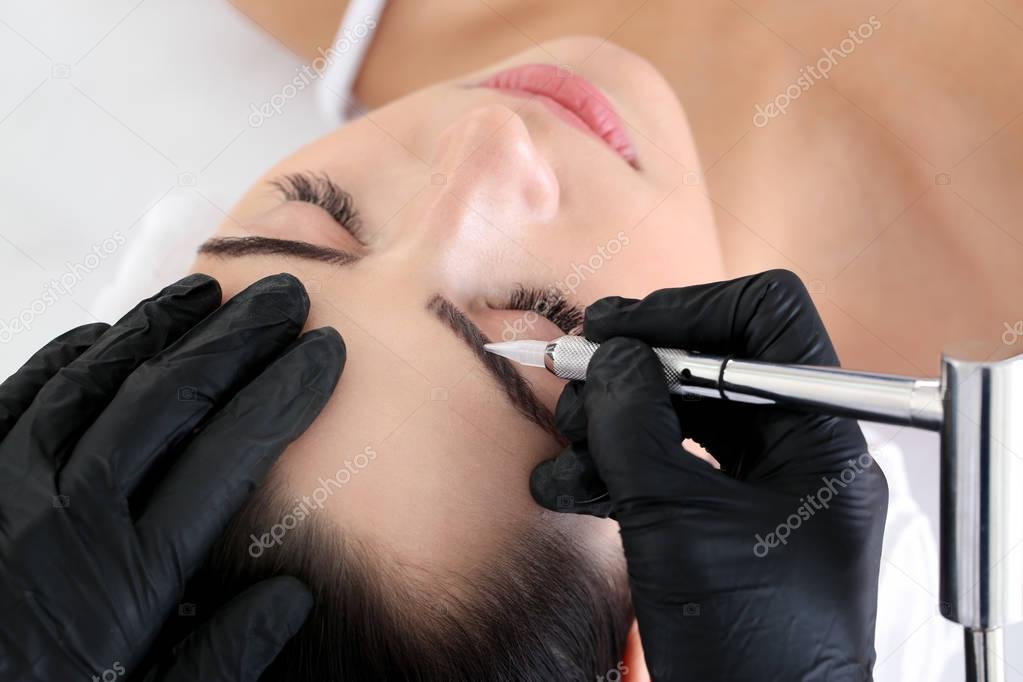 Young woman undergoing procedure of eyebrow permanent makeup in beauty salon, closeup