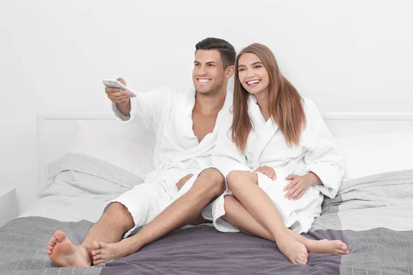 Unga älskande par i badrockar avkopplande på säng på hotel — Stockfoto