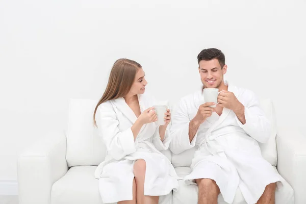 Young loving couple in bathrobes relaxing on sofa — Stock Photo, Image