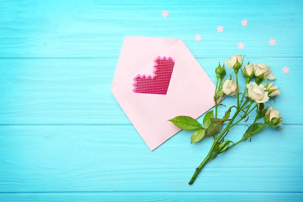 Plastic heart in envelope and roses on wooden background — Stock Photo, Image