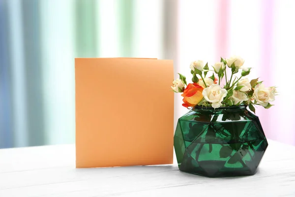 Vase mit Rosen und Blanko-Karte auf dem Tisch — Stockfoto