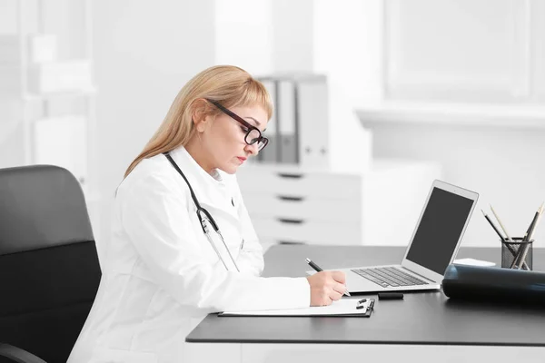 Médico femenino rellenando formulario de solicitud en sala de consulta —  Fotos de Stock