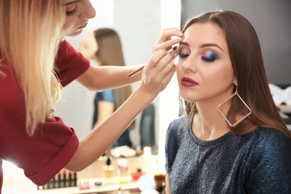 Professionell makeupartist arbetar med attraktiv ung kvinna inomhus — Stockfoto