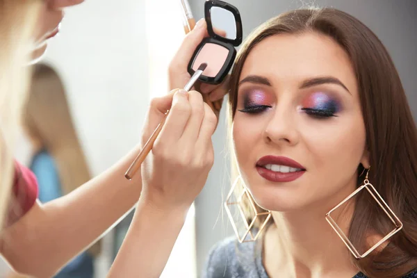 Artista de maquillaje profesional trabajando con atractiva mujer joven en el interior —  Fotos de Stock