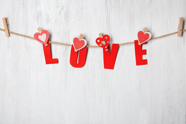 Woord liefde gemaakt papier briefwisseling met harten opknoping op touw tegen houten achtergrond — Stockfoto