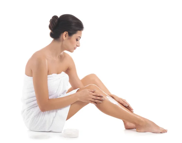 Νεαρή γυναίκα εφαρμογή κρέμα σώματος στο πόδι της ενάντια σε λευκό φόντο — Φωτογραφία Αρχείου