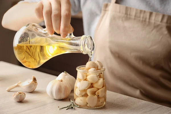 Vrouw olie gieten in pot met knoflook op tafel, close-up — Stockfoto