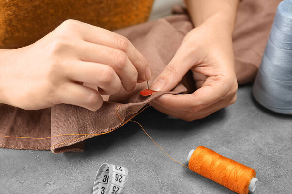 Seamstress sewing button on fabric at table in workshop