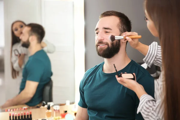 Professionell makeupartist arbetar med attraktiv ung man inomhus — Stockfoto