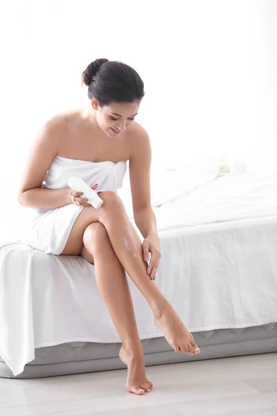 Mujer joven aplicando crema corporal en su pierna en el dormitorio — Foto de Stock