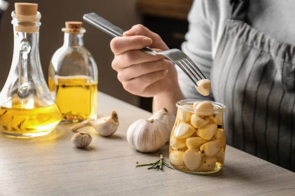 Vrouw probeert bewaard knoflook op tafel, close-up — Stockfoto