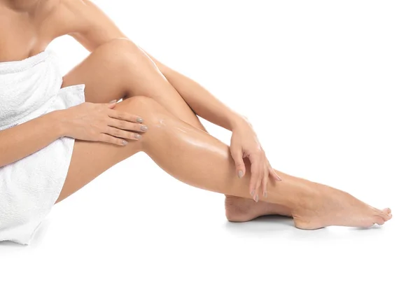 Kvinna applicera kroppskräm på hennes ben mot vit bakgrund, närbild — Stockfoto