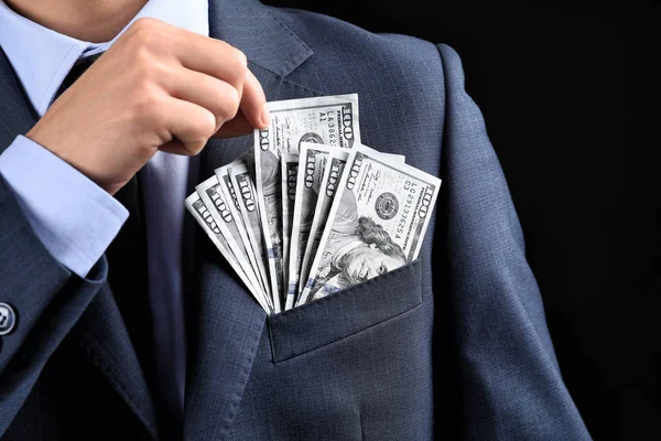 Businessman putting banknotes in pocket on dark background. Corruption concept — Stock Photo, Image