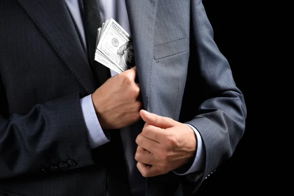 Businessman putting banknotes in pocket on dark background. Corruption concept — Stock Photo, Image