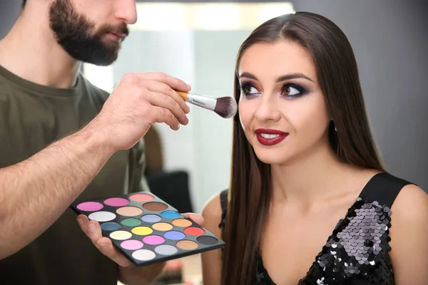 Professionell makeupartist arbetar med attraktiv ung kvinna inomhus — Stockfoto