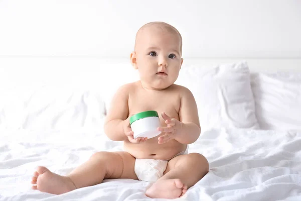 Cute baby with jar of body cream on bed — Stock Photo, Image