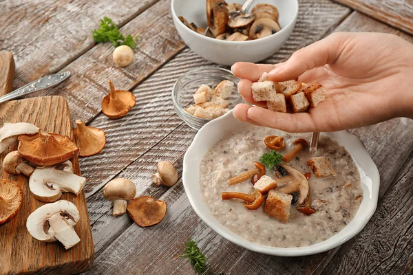 Junge Frau würzt köstliche Pilzsuppe am Holztisch mit Croutons — Stockfoto