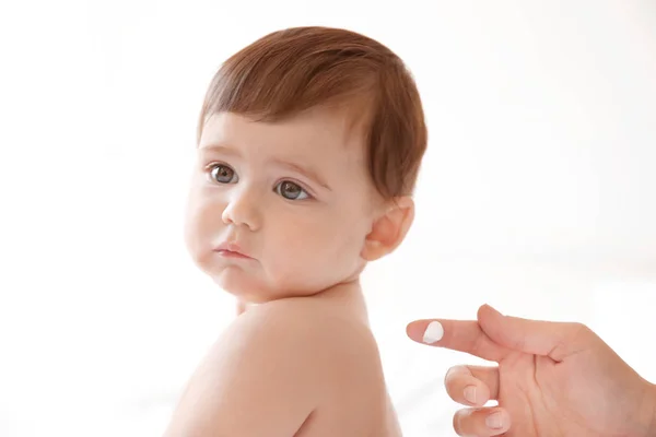 Mulher aplicando creme corporal em seu bebê contra fundo claro — Fotografia de Stock