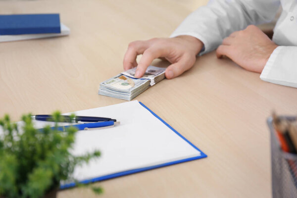 Мужчина-врач со взяткой на рабочем месте, крупный план
