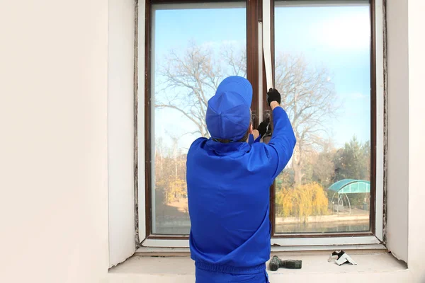 Construction worker removing sticky tape from window frame in house