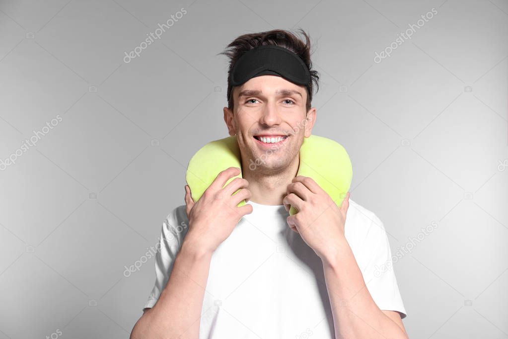 Young man with travel pillow and sleep mask on grey background